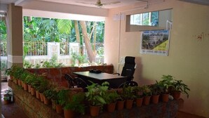 Una habitación con una mesa, sillas, plantas en macetas, un ventilador de techo y un cartel en la pared.