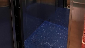 Interior de ascensor con paredes metálicas, piso azul y barandilla.