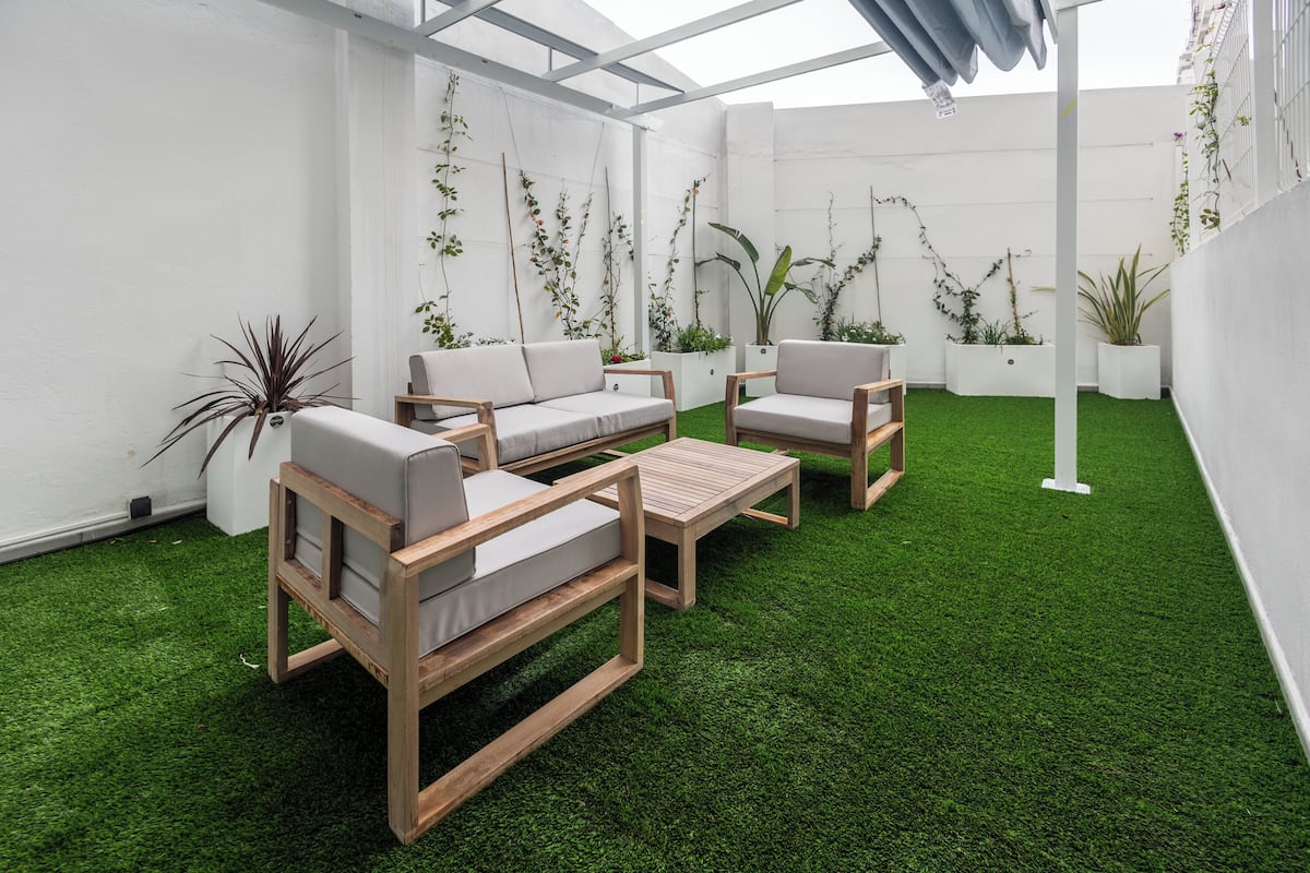 Une terrasse extérieure moderne, dotée de mobilier en bois et d’un gazon synthétique vert.