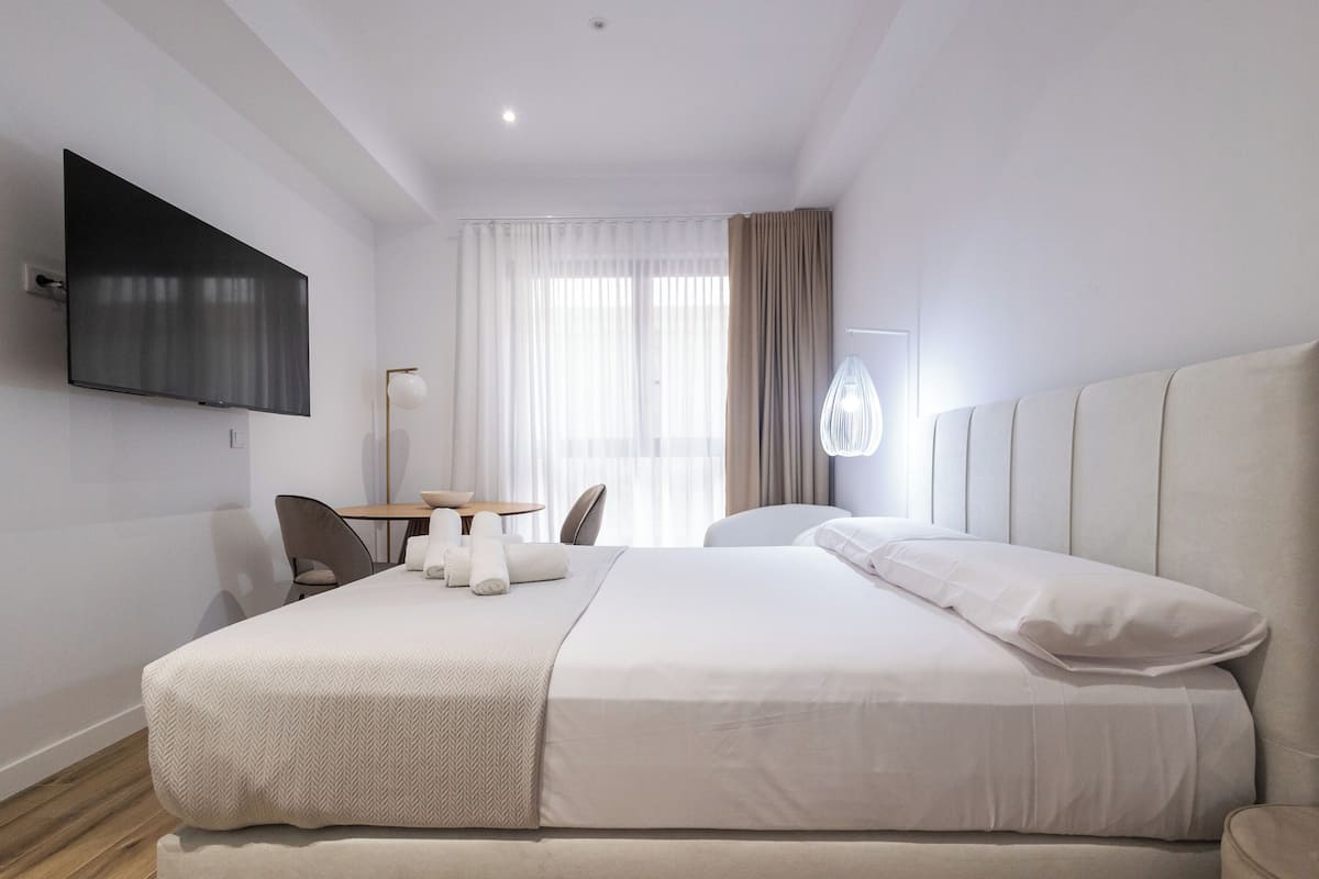Une chambre d’hôtel moderne dotée d’un grand lit, d’un téléviseur à écran plat fixé au mur, d’un bureau avec une chaise et d’une fenêtre avec des rideaux.