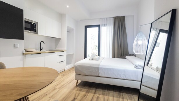 A modern bedroom with a bed, a bedside table, a mirror, and a view of the outdoors. - Lôla Suites by Concept (València)