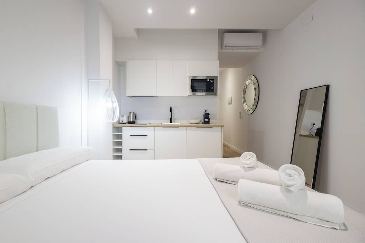 Une chambre d’hôtel moderne équipée d’un lit, d’une petite kitchenette, d’un miroir et de serviettes soigneusement pliées.