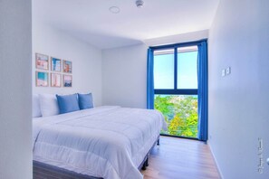 Un dormitorio con cama, ventana con cortinas azules y balcón con vegetación.