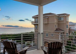 Un balcon avec des chaises donnant sur une vue imprenable sur la mer, un bâtiment avec un toit en tuiles et un ciel dégagé.