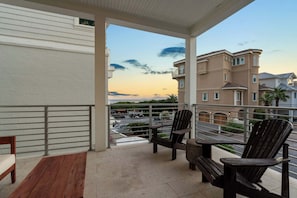 A balcony with wooden furniture, a view of a parking lot, and buildings in the background.