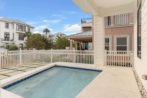 A swimming pool with a white fence, a covered patio, and a view of neighboring houses.