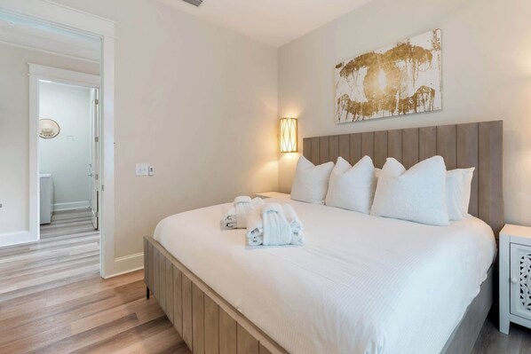 A hotel room with a large bed, a headboard, a bedside table, and a wall-mounted artwork.