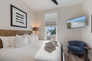 A hotel room with a large bed, a TV, a chair, and a view of the beach.
