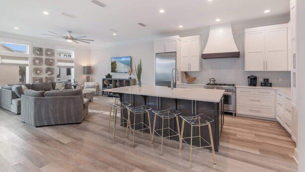 A modern kitchen with a central island, bar stools, and a dining area with a sofa. - NEW "Bikinis & Martinis" Private Pool,Gulf Views, Bikes, LSV (Santa Rosa Beach)
