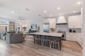 A modern kitchen with a central island, bar stools, and a dining area with a sofa.
