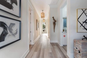 A hallway with wooden flooring, framed artwork on the walls, a decorative light fixture, and a fire safety sign.