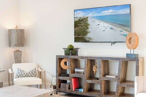 A living room with a beach view, a mounted TV, and a wooden console with books and decorative items.