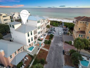 A multi-story hotel with a swimming pool, a parking area, and a view of the beach.