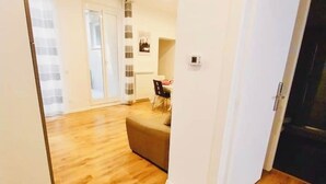 A room with wooden flooring, a sofa, a dining table with chairs, and a door leading to another room. - La Dimora di Sara - Comfort and Privacy at 10 Minutes from Termini (Roma)