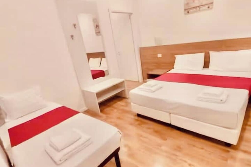 A hotel room with a bed, a bedside table, and a mirror.