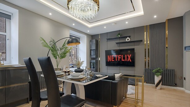 A modern living room with a dining area, a TV displaying 'NETFLIX,' and a chandelier. - Jackson Terrace HL6 - Grampian Lettings (Aberdeen)