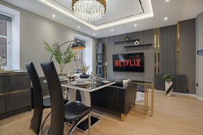 A modern living room with a dining area, a TV displaying 'NETFLIX,' and a chandelier. - Jackson Terrace HL6 - Grampian Lettings (Aberdeen)