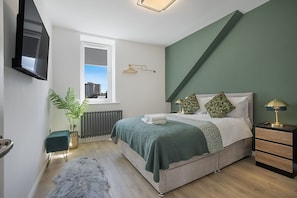 A modern bedroom with a bed, bedside tables, a radiator, a window, and a plant.
