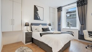 A modern bedroom with a large bed, bedside tables, a wardrobe, a window with curtains, and a view of the outside. - Jackson Terrace HL6 - Grampian Lettings (Aberdeen)
