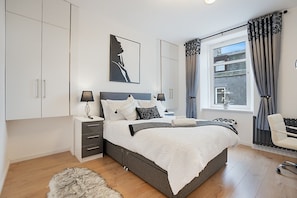 A bedroom with a large bed, bedside tables, a wardrobe, a window with curtains, and a view of the outside.