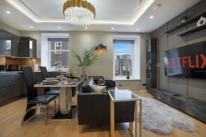 A modern living room with a dining area, a TV displaying 'NETFLIX,' and a large window.