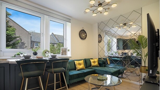 Uma sala de estar moderna com um sofá verde, uma mesa de centro de vidro e uma área de cozinha com um banco de bar.