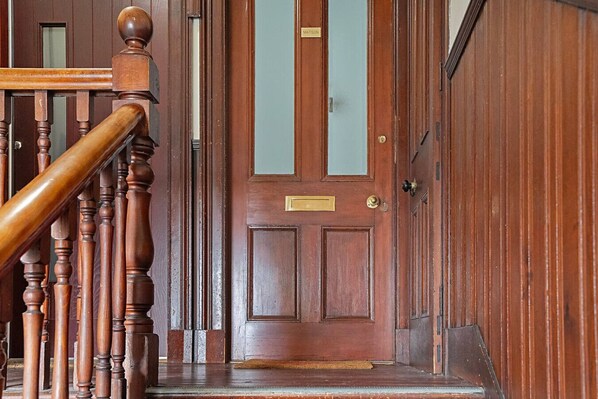 A wooden staircase leading to a door with a brass plate, a glass panel, and a brass doorknob.