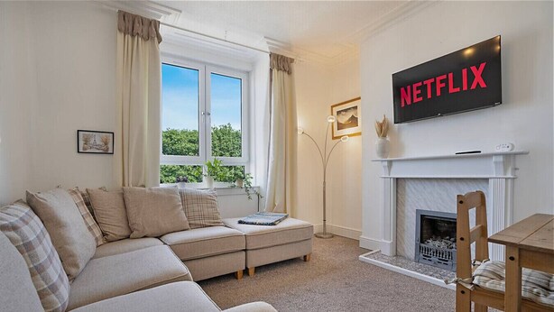 A living room with a sofa, a fireplace, a table, and a TV displaying 'NETFLIX'. - Abbey Place Apartment | Grampian Lettings (Aberdeen)