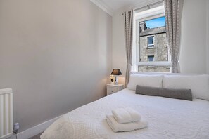 Una camera da letto con un letto, un comodino con una lampada, una finestra con tende e vista su un edificio in pietra.
