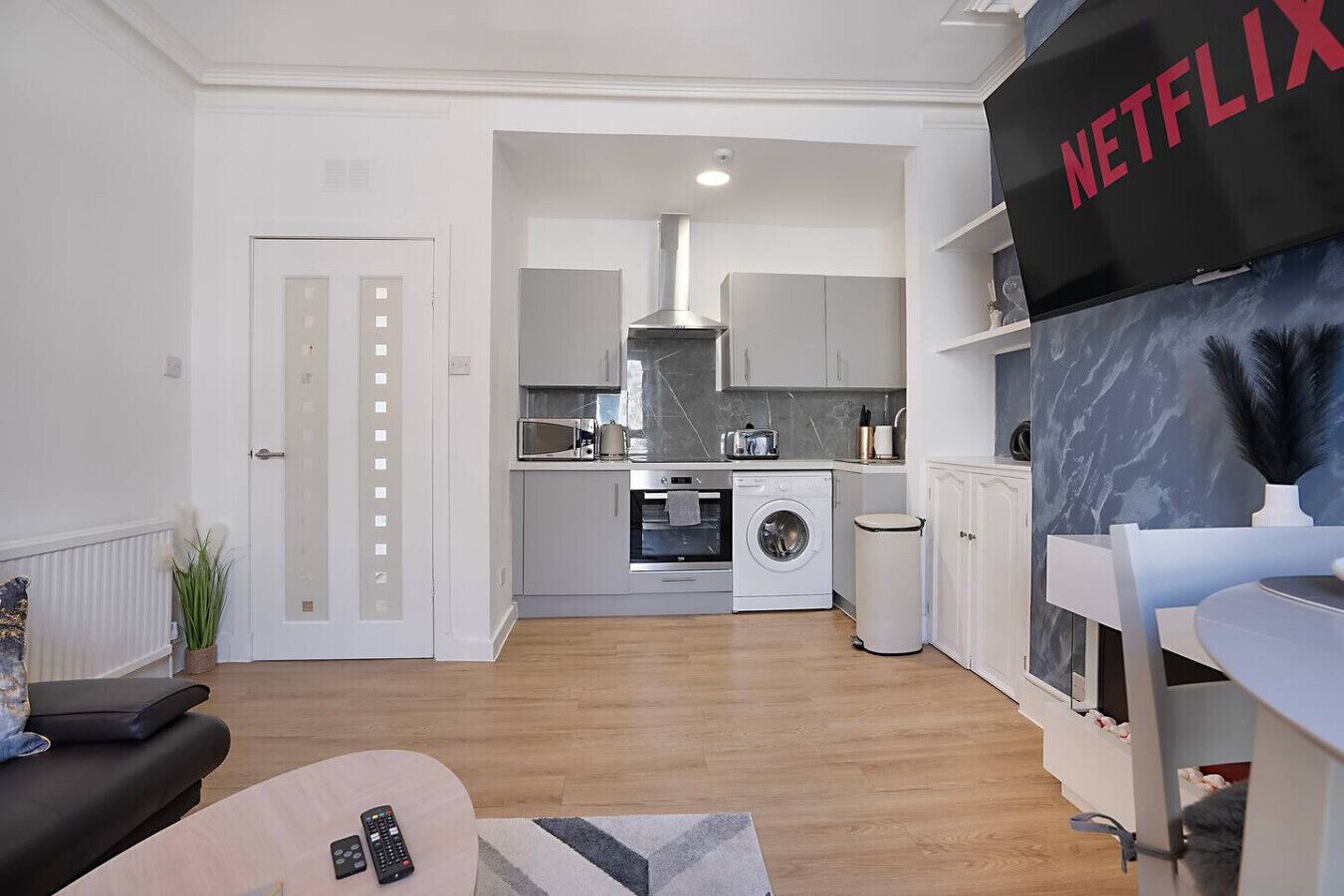 Een modern appartement met een keuken, woonruimte en een televisie met Netflix logo.