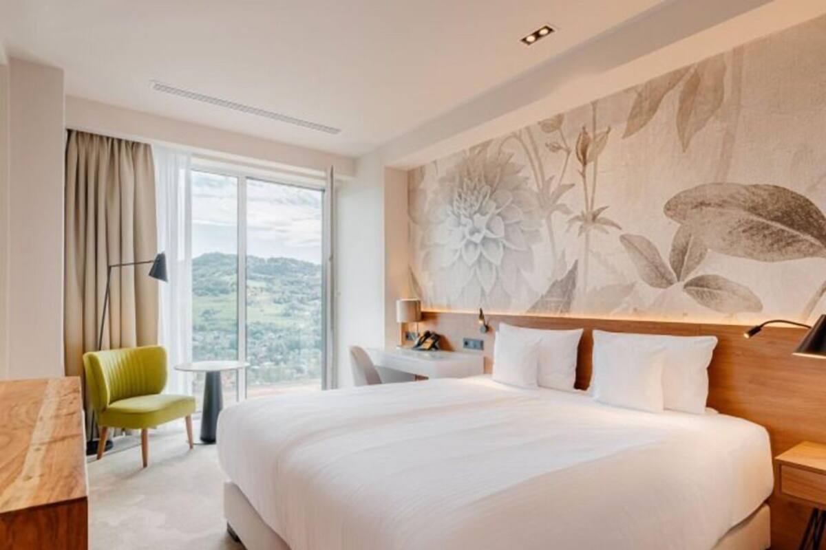 A hotel room with a large bed, a desk, a chair, and a view of the outdoors.