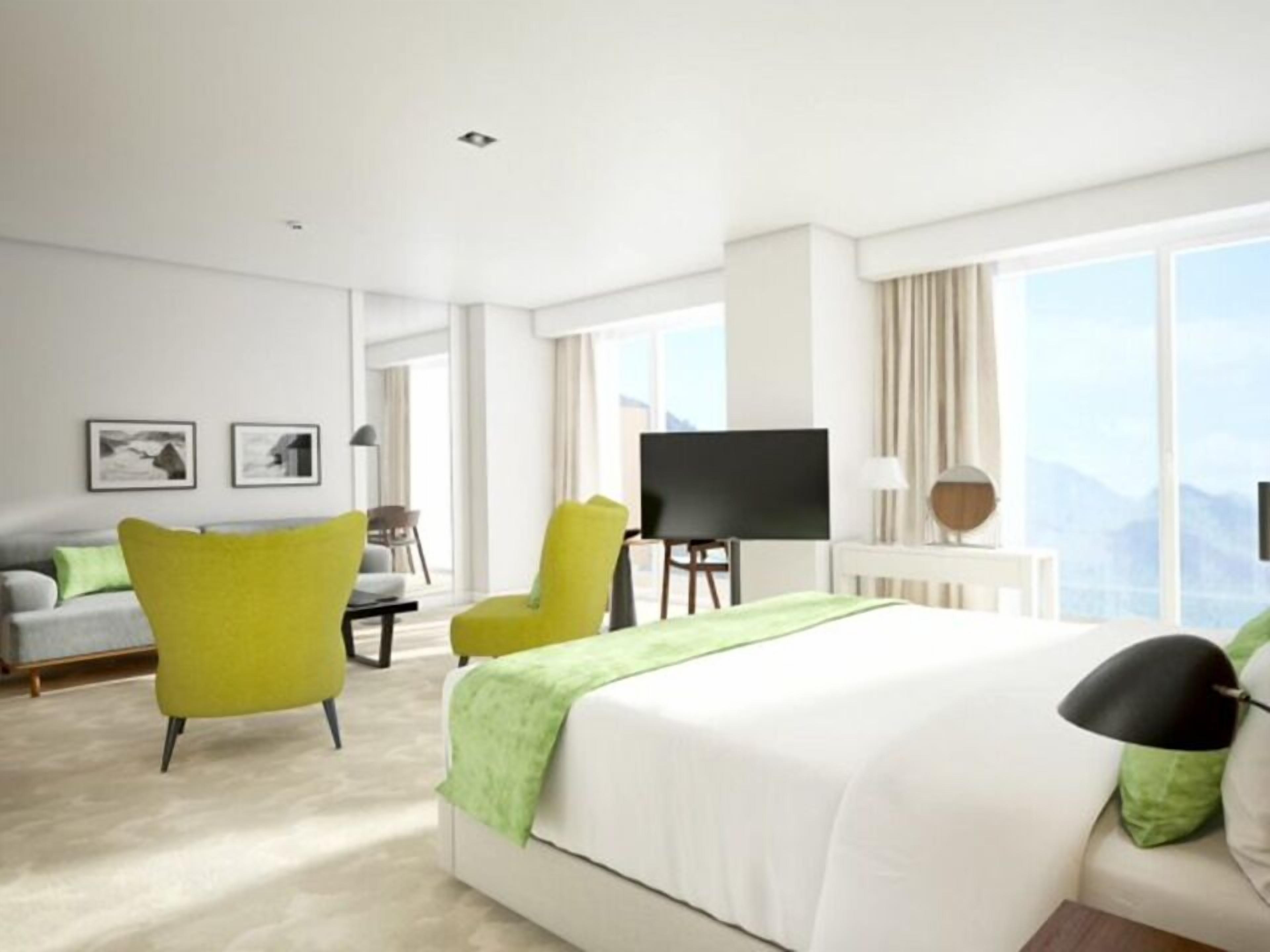 Una habitación de hotel moderna con una cama grande, un televisor de pantalla plana, un escritorio y vistas a las montañas a través de las ventanas.