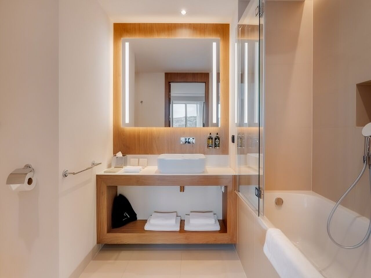 A modern bathroom with a wooden vanity, a large mirror, and a glass shower enclosure.