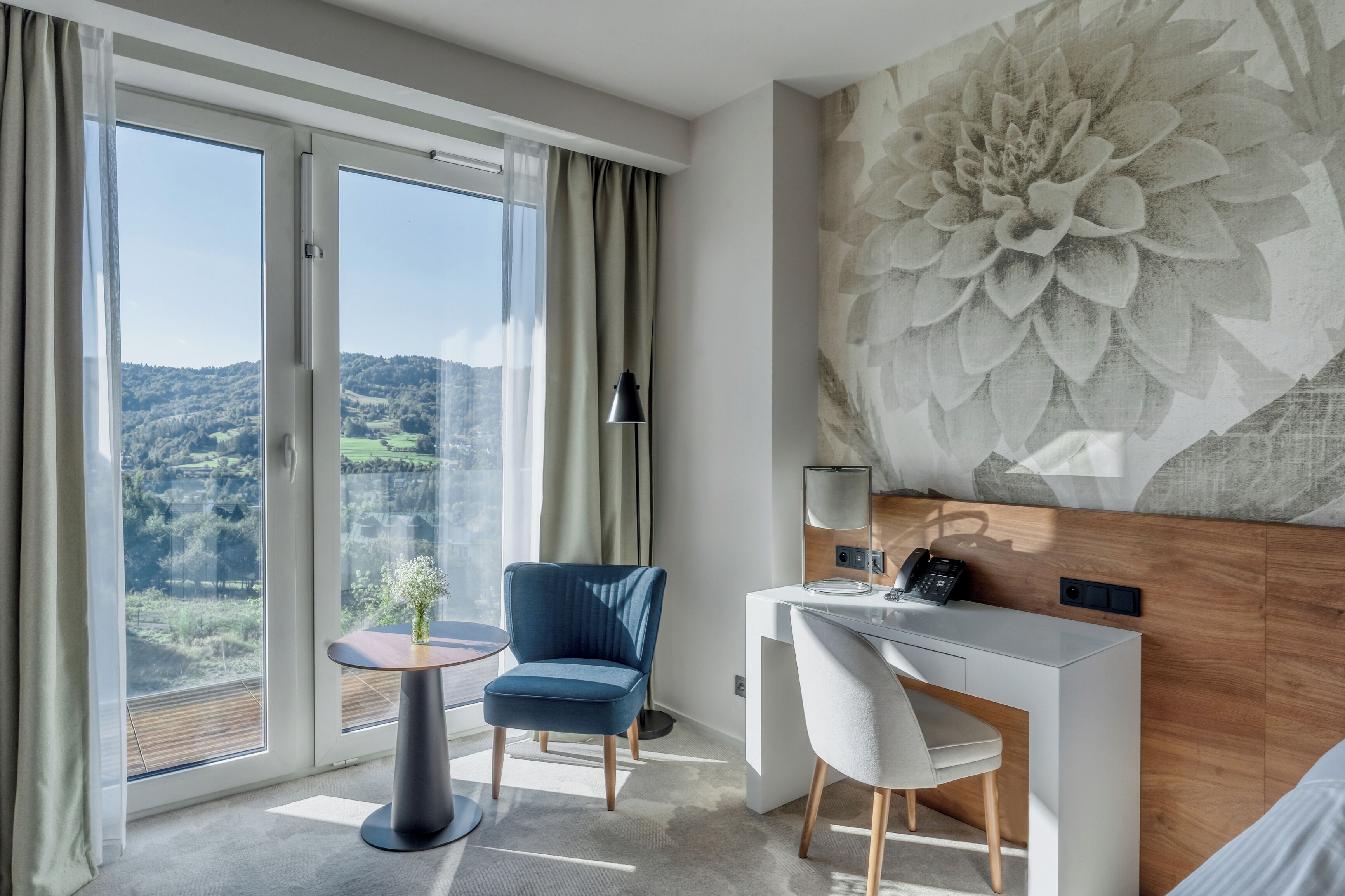 Una habitación de hotel moderna con un ventanal grande, un escritorio, una silla y un adorno en la pared.