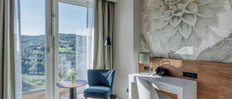 Una habitación de hotel moderna con un ventanal grande, un escritorio, una silla y un adorno en la pared.