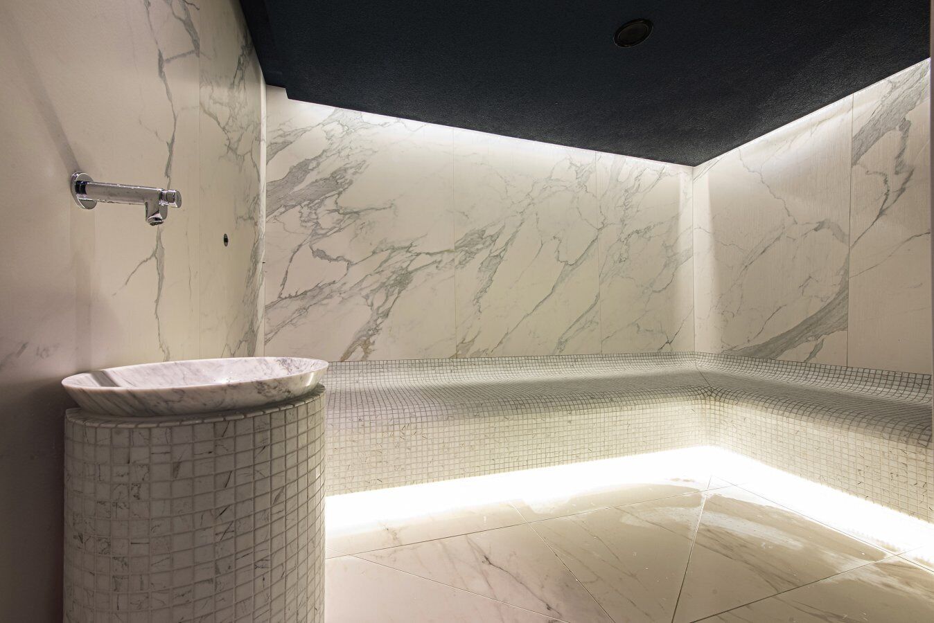 A modern bathroom with a marble wall, a freestanding sink, and a corner bathtub.