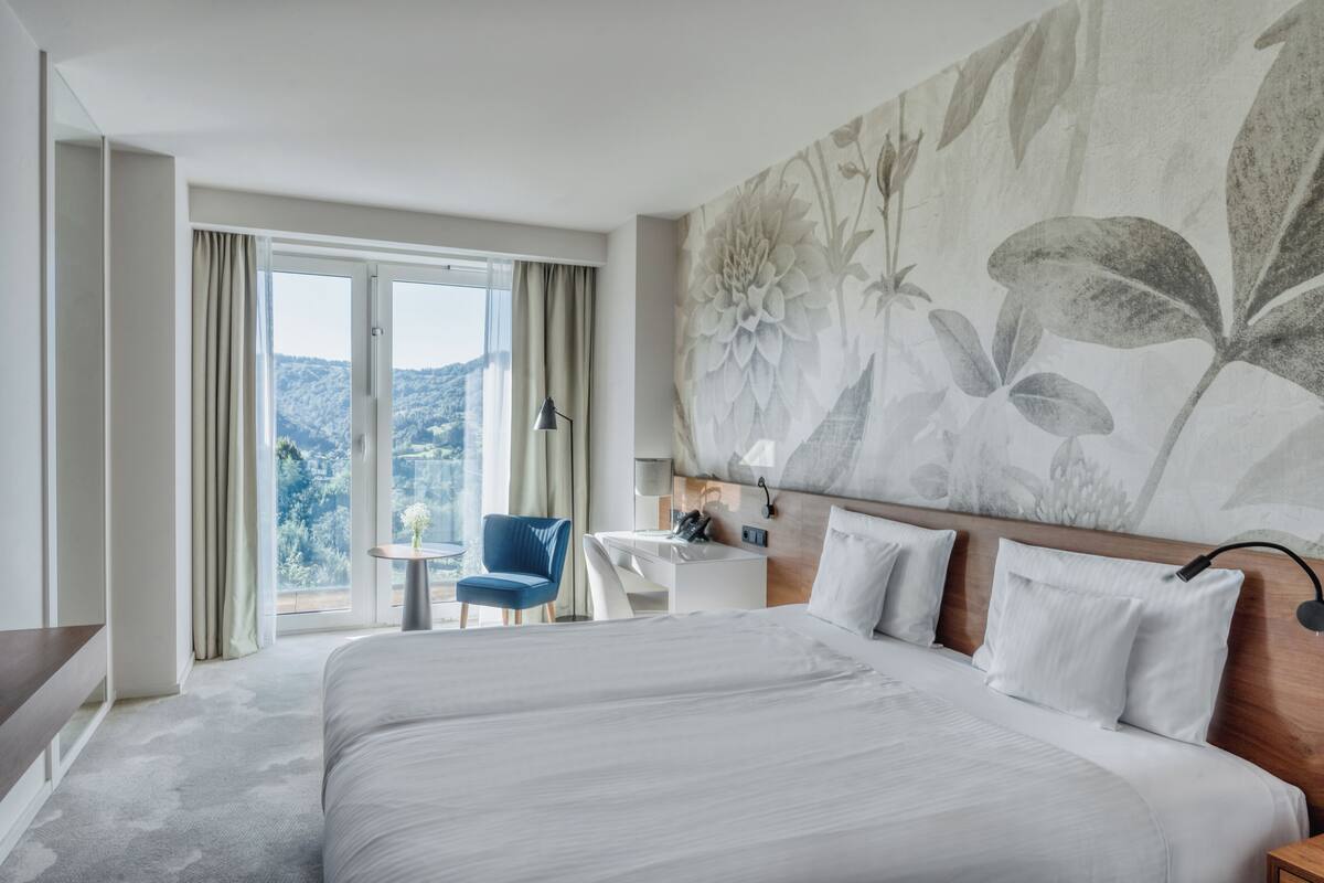 A hotel room with a large bed, a desk, a chair, and a view of the outdoors.