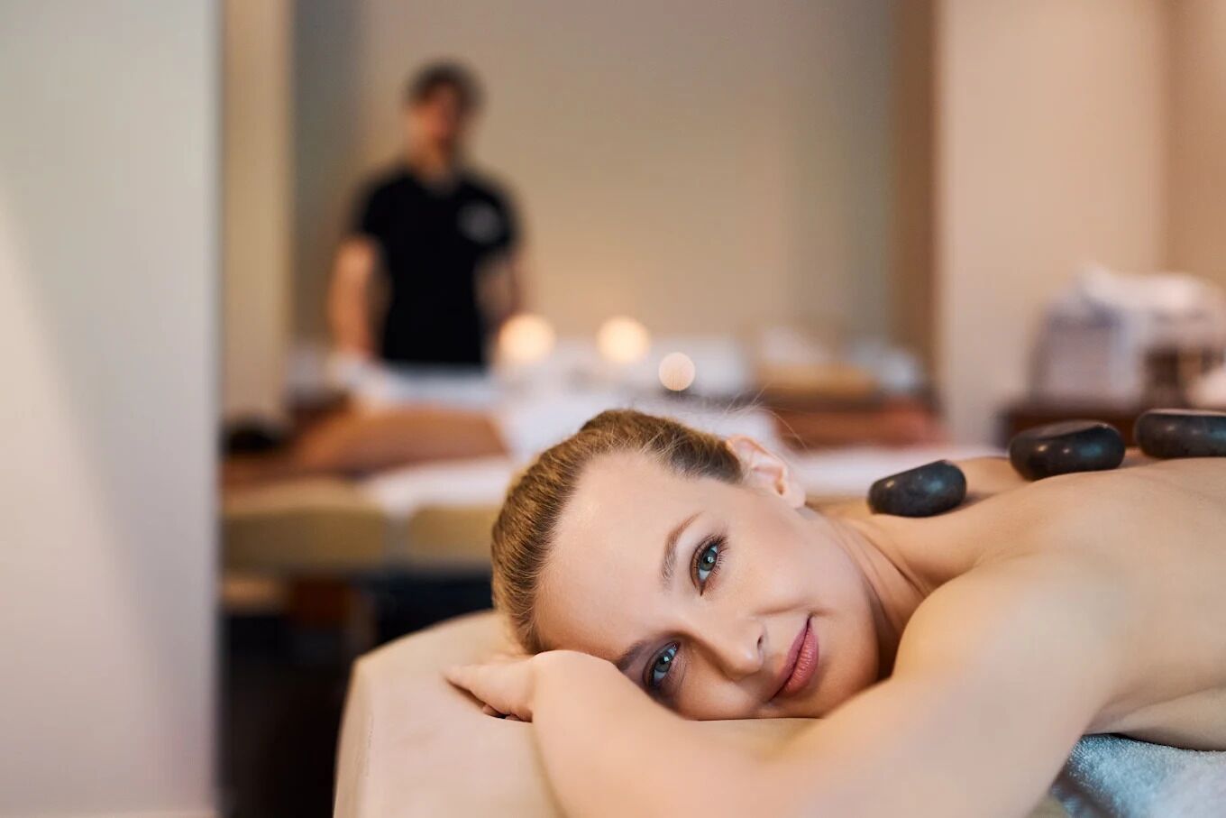 Une personne reçoit un massage, et on aperçoit un thérapeute en arrière-plan.