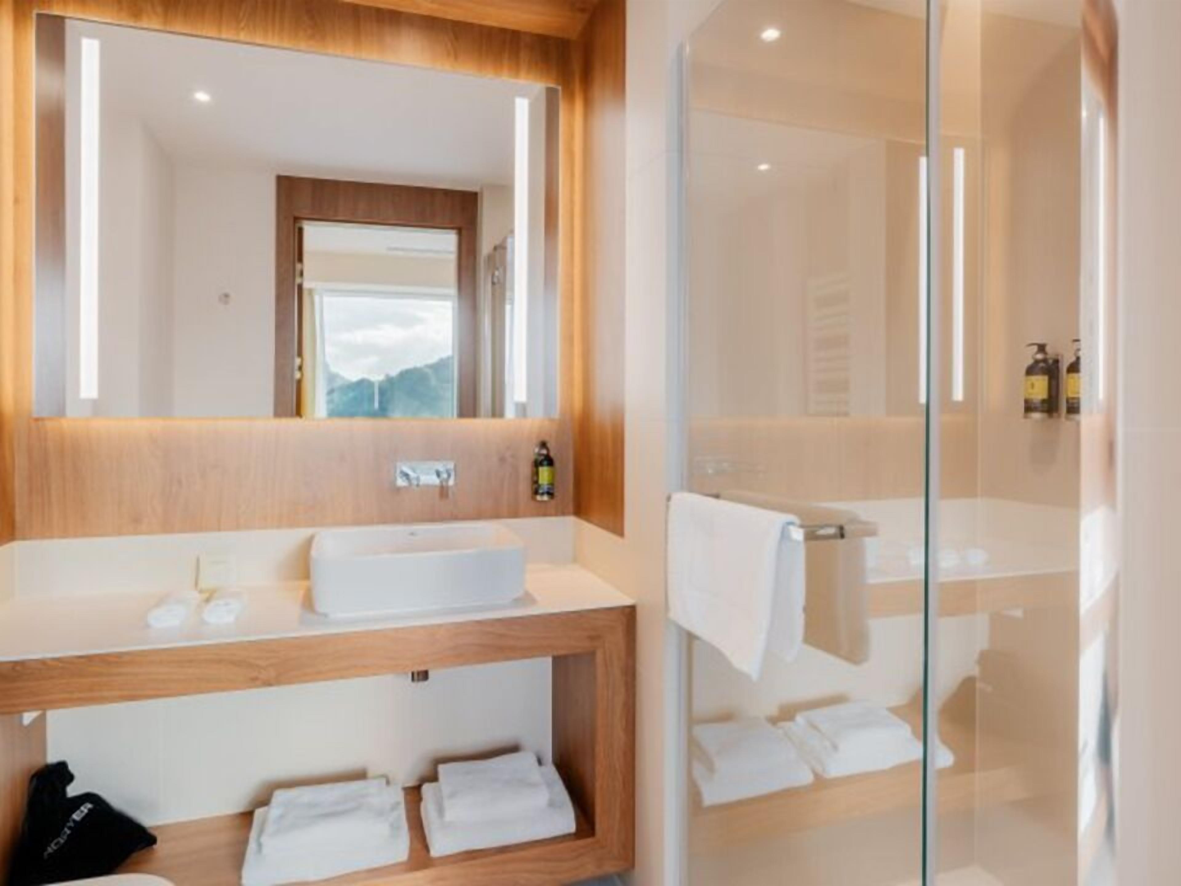 Un baño moderno con tocador de madera, un espejo grande y zona de ducha con mampara de vidrio.