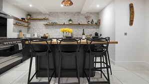 A modern kitchen with a central island, black bar stools, and a hanging pendant light.