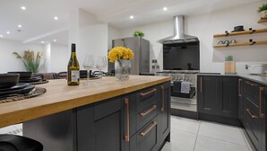 A modern kitchen with dark cabinetry, a wooden island, stainless steel appliances, and a hanging plant.
