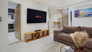 A modern living room with a flat-screen TV mounted on the wall, a wooden console table, a brown sofa, and a staircase leading to another level.