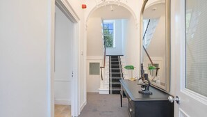 Un couloir avec un escalier, un bureau avec une lampe et un grand miroir.