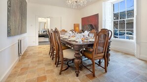 Une salle à manger avec une grande table, des chaises, un lustre et une fenêtre donnant sur un beau paysage.