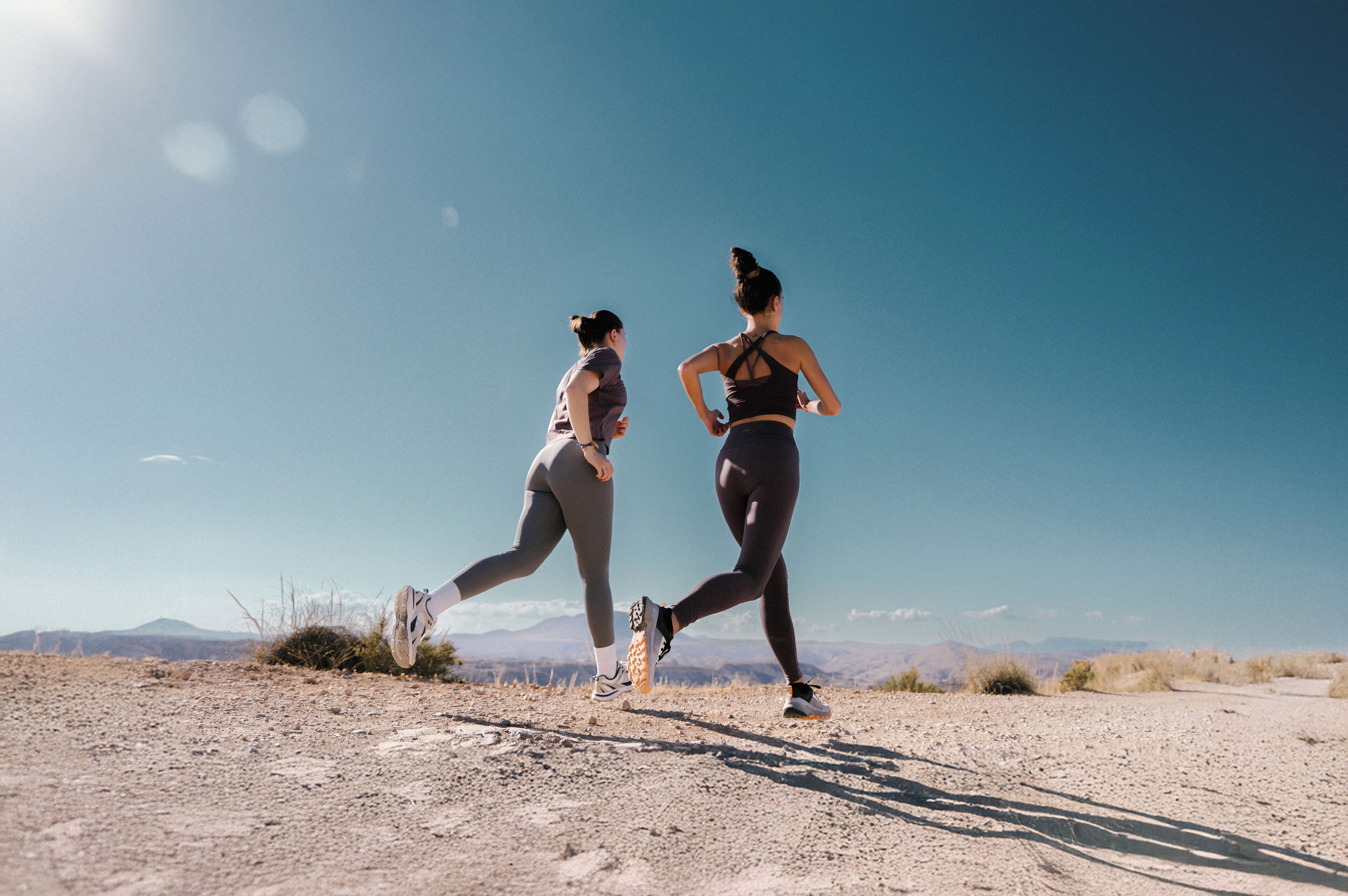 Two people running on a dirt path with a clear sky and distant mountains.