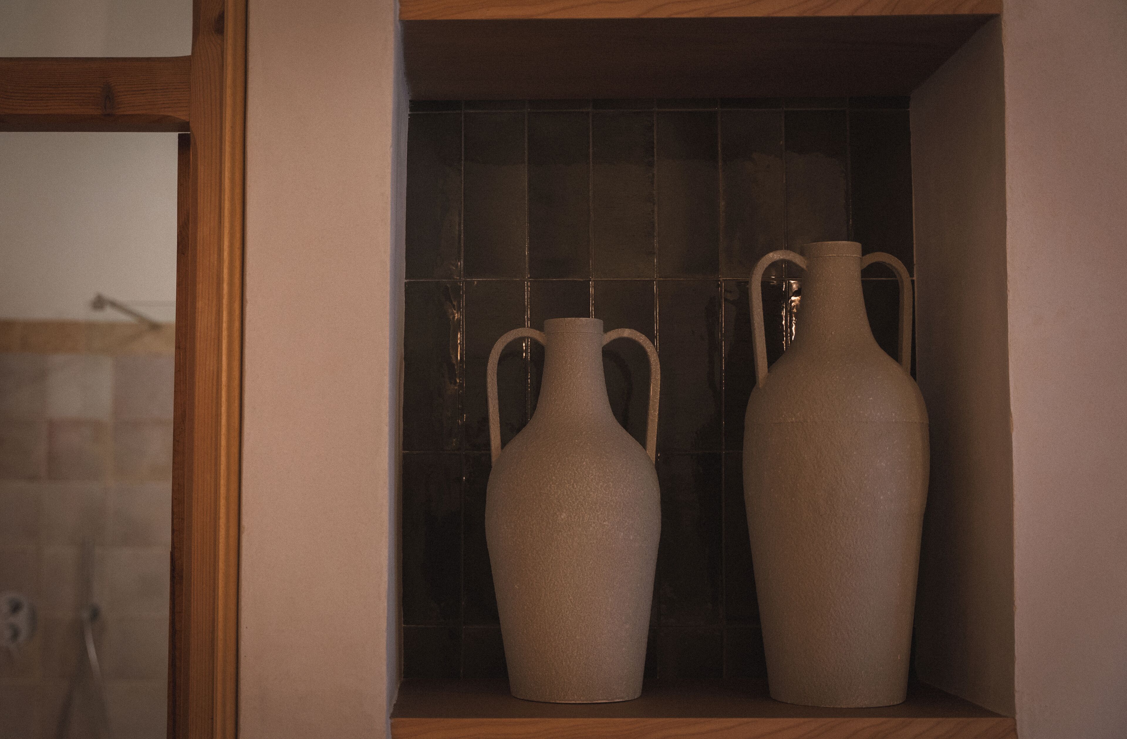 Two ceramic vases on a shelf with a tiled backsplash.