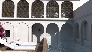 A poolside area with lounge chairs, a water feature, and arched windows. - Hotel Boutique Casona de los Rebolledo (Zújar)