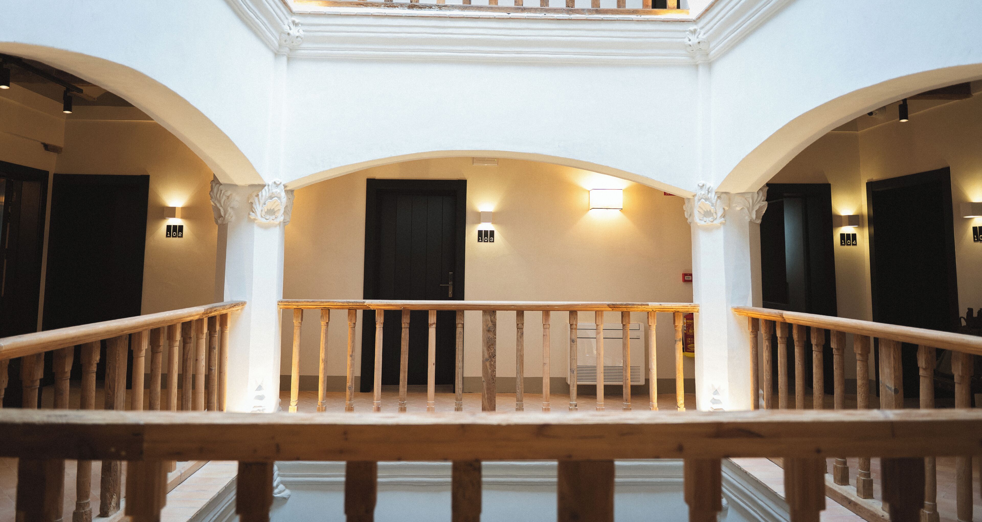 Un magnifique escalier en bois, agrémenté de rampes, flanqué de murs blancs et d’ouvertures en arc, menant à de nombreuses pièces.