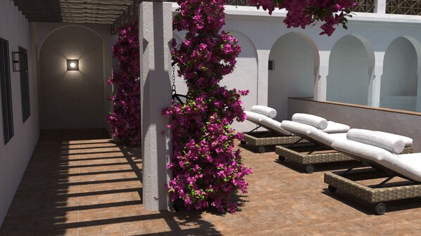 Zona exterior soleada con sillones de descanso y una pared decorada con plantas en flor.