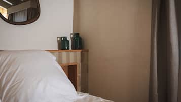 Un dormitorio con cama, una estantería de madera con dos jarras verdes y un espejo en la pared.